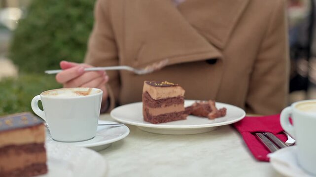 Woman enjoying chocolate layer cake at outdoor cafe terrace during cold day.