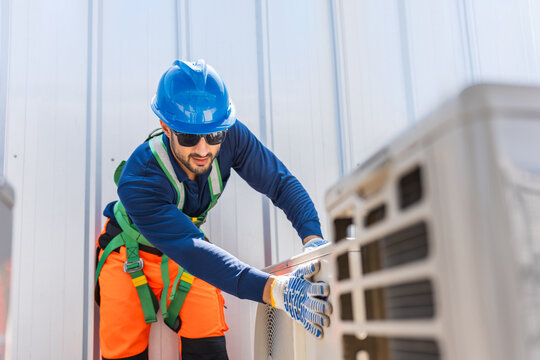 HVAC technician checking air conditioning condenser unit on rooftop during maintenance, Technician man performing quality check on industrial air conditioning unit on rooftop exterior