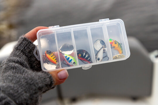 Hand holding a clear tackle box filled with fishing lures spinner tail
