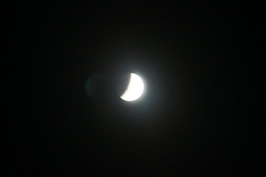 Glowing partial lunar eclipse in the pitch black dark night sky with a subtle lens flare