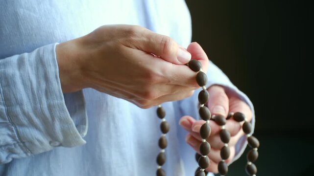 Close up woman hands moving along string japa mala beads, spiritual practice prayer, meditation, mantra repetition to find inner peace and mindfulness. Hands praying with traditional japa mala beads
