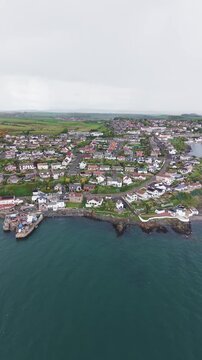 Panoramic aerial view of Pettycur Bay and harbour in Burntisland, Fife, Scotland. Scenic vertical drone shot capturing the traditional coastal village houses, rugged shoreline, and the calm blue water