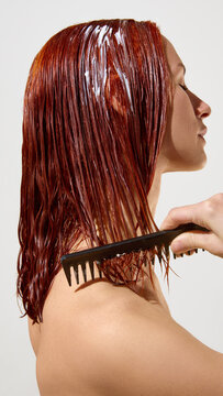 Woman combing copper red hair mask through wet strands in studio profile. Concept of deep conditioning, detangling, color repair, salon treatment and haircare product demo.