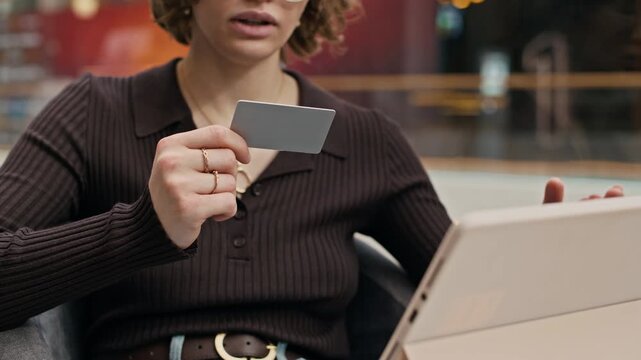 Cropped slowmo shot of focused young girl sitting in mall lounge and using credit card while making online payment on digital tablet