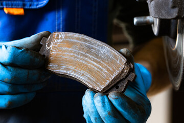 An old worn brake pad in the male hands of an auto repairman at a service station. © Юлия Черкасова