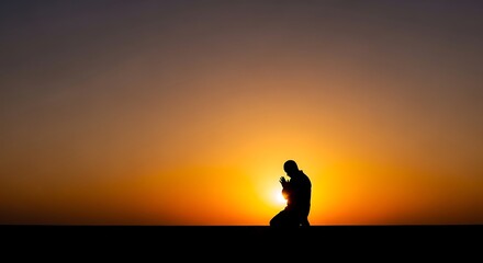 Silhouette of a man kneeling in prayer against a vibrant sunset sky