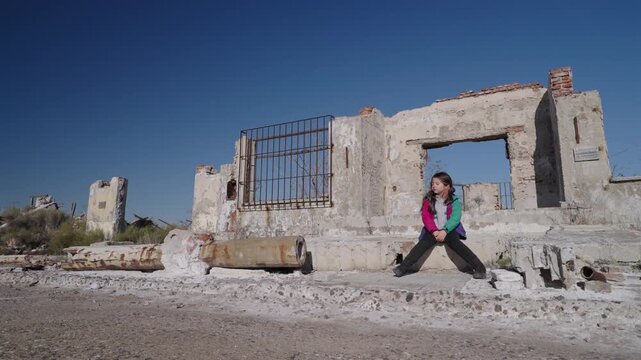 Sad lone Child seated in ruined structure in salinized landscape likely after climate driven flooding and long term evaporation showing ecological collapse abandonment and isolation, static wide shot