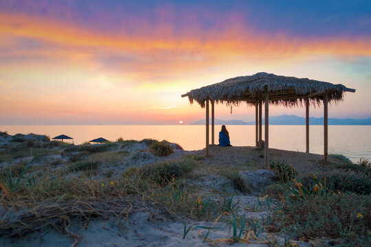 sunset beach with a woman sitting in a gazebo pavilion in Greece watching the sunset in the aegean sea