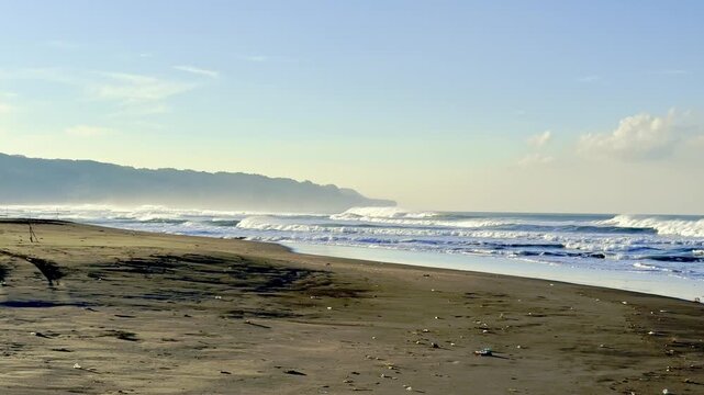 Wide tropical beach with distant headland and waves