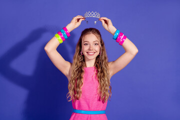 Youthful girl in a pink dress holding a tiara against a purple background, showcasing playful elegance and trendy style © deagreez