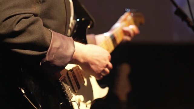 Guitarist playing electric guitar during rock concert. Close-up of man's hands playing stringed musical instrument.