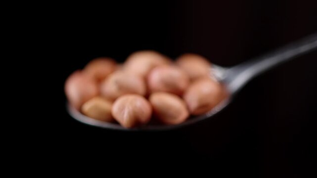 4k slow motion shot of Indian peanuts or groundnuts, kept on a spoon with black background, shot with professional studio lighting and camera setup, showing a portion recommended for nutrition