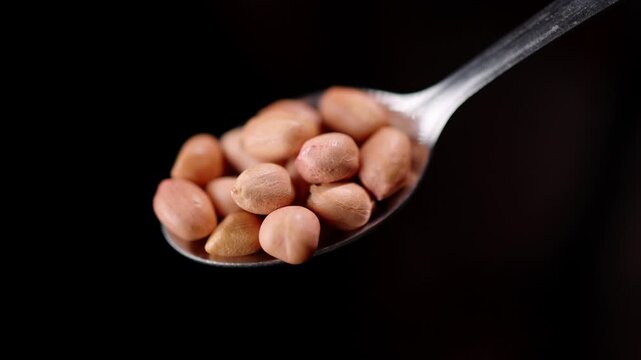 4k slow motion shot of Indian peanuts or groundnuts, kept on a spoon with black background, shot with professional studio lighting and camera setup, showing a portion recommended for nutrition