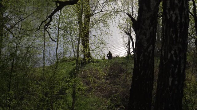Wide shot man fishing in the pond or river. Adult man fisherman in cap with a fishing rod from shore on small lake near reed.