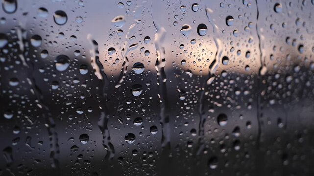 Raindrops sliding slowly down window glass at twilight
