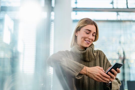 Smiling young woman sitting in waiting area using cell phone