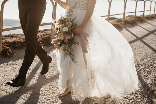 Close-up of bride and groom walking on path at the coast
