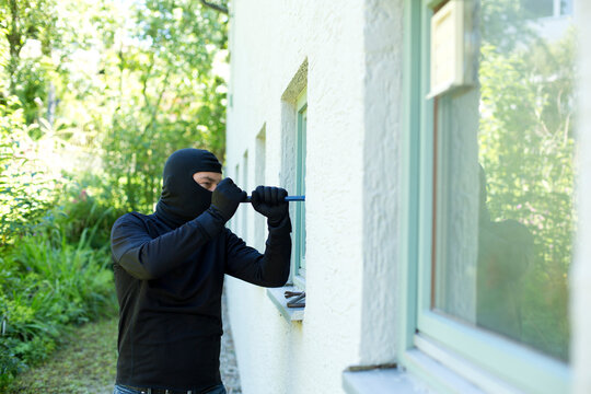 Burglar with crowbar breaking window