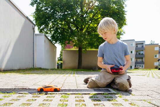 Boy playing with remote controlled car in yard outside garage