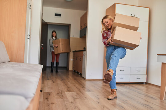 Two young women carrying cardboard boxes into a room