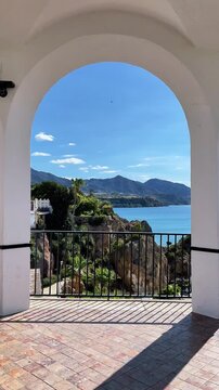 Scenic view of the Mediterranean sea and mountains through a white arch at Balcon de Europa in Nerja, Andalusia, Spain, beautiful coastal landscape and traditional Spanish architecture on a sunny day.