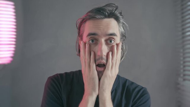 surprise shock hand face misunderstanding A bearded man gray background softly lit by pinkish-purple light, showing shifting expressions from puzzled to astonished covering face shock disbelief