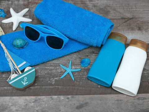  Beach accessories, including sunscreen, sunglasses, and a towel, on a wooden background.