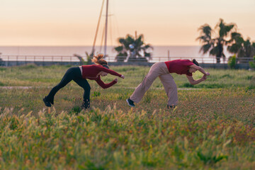 Two active women practicing contemporary dance and expressive movement in a grassy field at sunset. © sirbouman