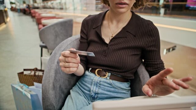 Cropped midsection shot of young girl sitting in mall lounge and inserting credit card numbers while making online payment on digital tablet