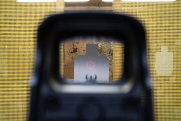First-person view through a holographic sight with sharp focus on a cardboard torso silhouette target at an indoor shooting range. © Dmitri