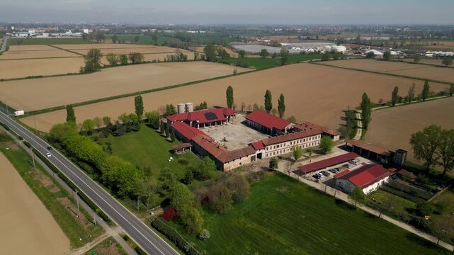 Italian farm surrounded by agricultural fields with a nearby road and light traffic. Rural landscape showing farming activity and regional transport.