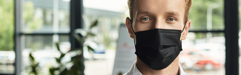 Young man in a black mask stands confidently indoors, natural light accentuating his features © LIGHTFIELD STUDIOS