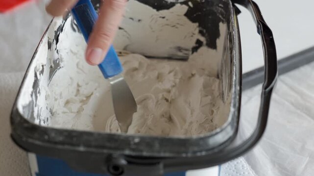 Artist mixes plaster putty in a container with a palette knife. Concept of textured wall art and DIY handmade decor.