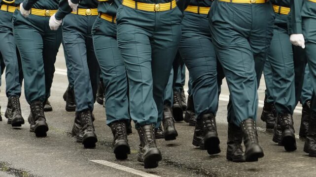 Close-up view of uniformed personnel marching in tight formation during a ceremonial parade, highlighting synchronized footsteps, black boots, green trousers on a damp street.