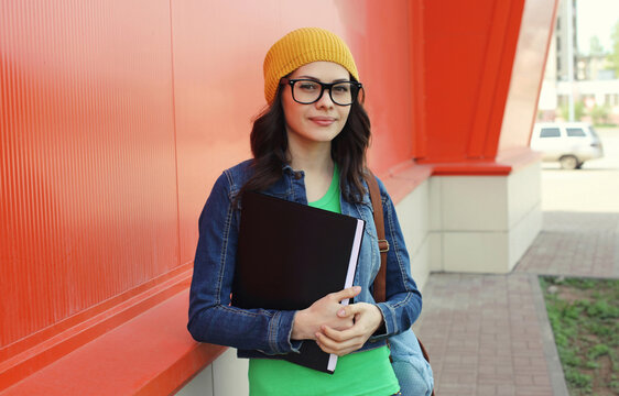 Happy woman student with eyeglasses, backpack standing in the city