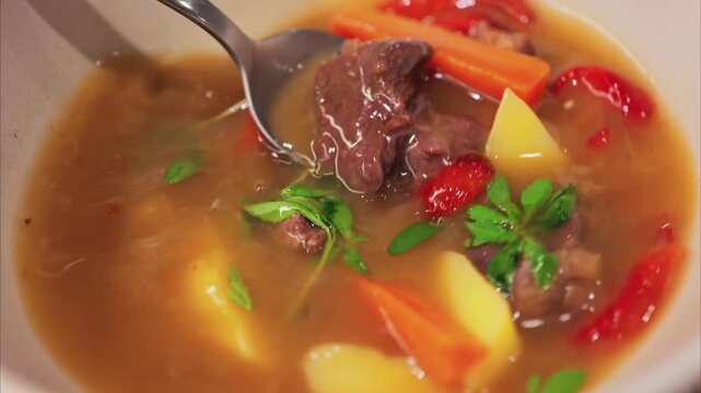 Stirring hearty beef stew with vegetables in a white bowl.