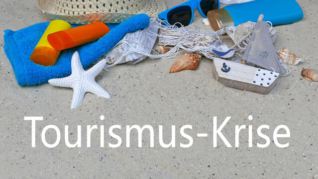 Reisebranche in der Krise: Strand mit Urlaubsaccessoires und dem Schriftzug Tourismus-Krise in den Sand geschrieben.