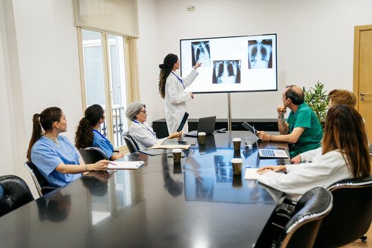 Healthcare professionals analyzing chest x rays on a screen, sitting around a conference table during a hospital meeting