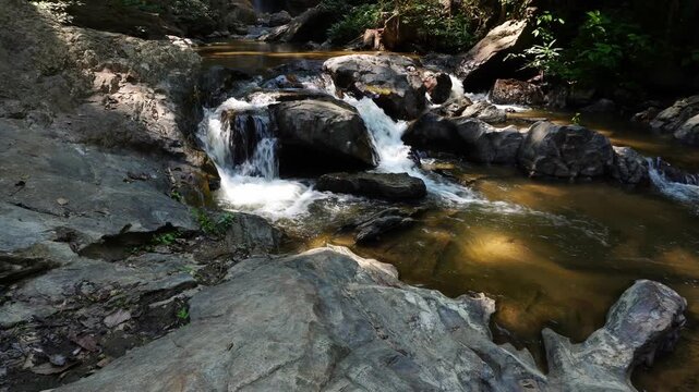 Beautiful reveal shot of Mork Fa waterfall in Chiang Mai, Thailand. Real-time zoom out and tilt up from fresh stream flowing through rocks to majestic cascade in jungle.