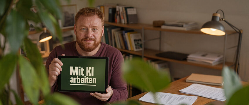 Klassisch deutscher rothaariger Mann h&auml;lt Tablet Mit KI arbeiten in Bibliothek breite Aufnahme &ndash; K&uuml;nstliche Intelligenz designtes Display