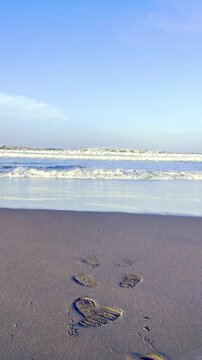Footprints in sand leading toward ocean waves