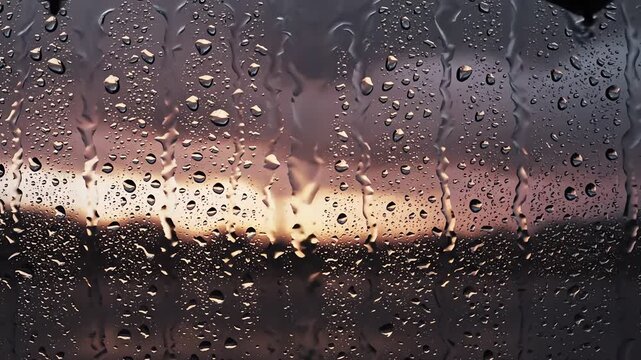 Raindrops sliding down window glass against sunset sky