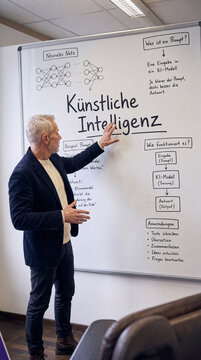 Klassisch deutscher Senior im Blazer zeigt auf Whiteboard K&uuml;nstliche Intelligenz mit Mindmap &ndash; KI Konzept Wissensvisualisierung Dozent Senioren