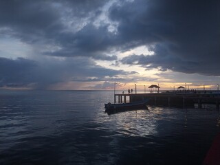 Obraz premium Dramatic Sunset Over the Ocean Pier with Boat and Stormy Clouds
