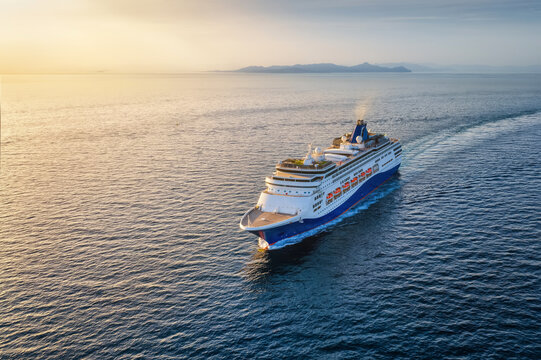 Aerial view of a cruise or passenger ship sailing over the calm ocean into the golden sunset with copy space