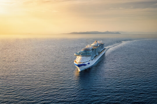 Aerial view of a cruise or passenger ship sailing over the calm ocean into the golden sunset with copy space
