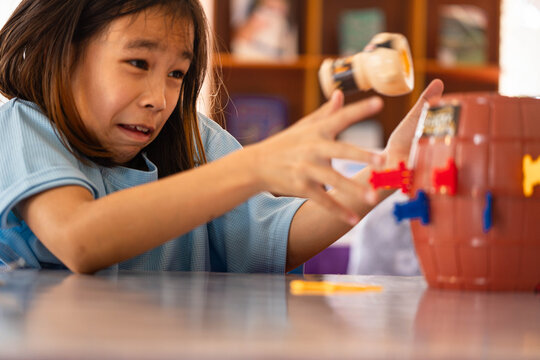 Excited little girl flinching as the pirate pops up while playing a classic barrel board game at home.