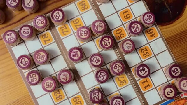 Vintage lotto game barrels with engraved numbers on old bingo cards over rustic wooden table filmed in descending handheld overhead shot from wide tabletop composition into extreme macro close up