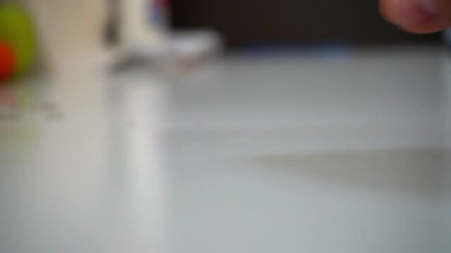A close-up shot of a single white pill rolling into the frame on a white surface, where a hand picks it up, symbolizing medication, healthcare, or daily health routines.