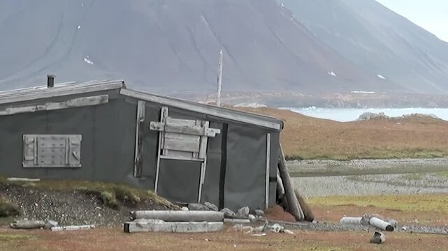 A lone, weathered hut stands resilient amidst the rugged Arctic landscape of Svalbard, Norway.